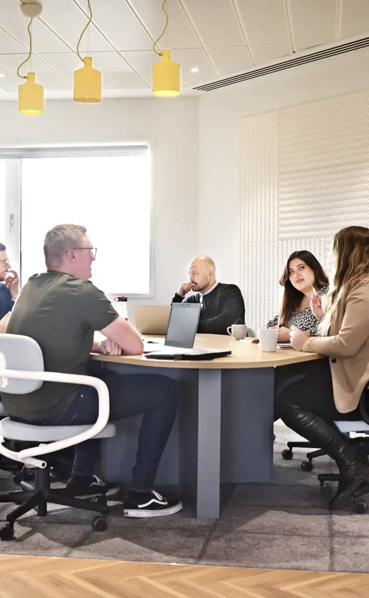 Six colleagues sit around a desk in an office