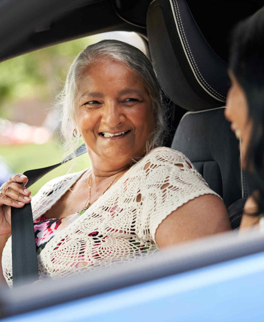 An older woman smiling and talking to a younger woman, inside a car