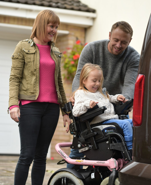 A man and woman smiling while helping a young girl in a wheelchair