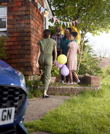 A woman is greeted as she arrives at a party, on the doorstop of a house with balloons