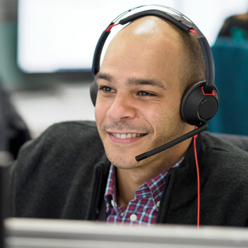 A smiling man with a headset on the phone in an office