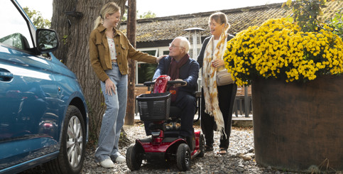 An older man on a mobility scooter looking and talking to a girl and a woman