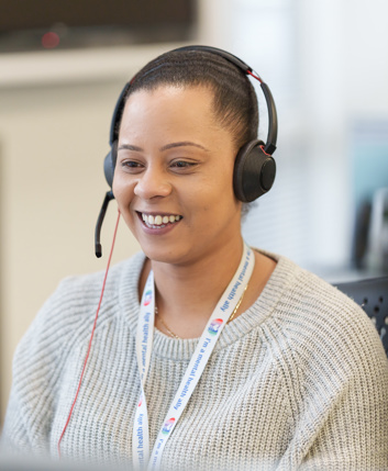 A smiling woman talking on a headset, in an office