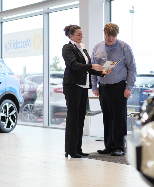 A dealer shows a man a booklet, in a dealership