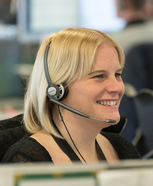A woman laughing while she talks on a headset, in an office