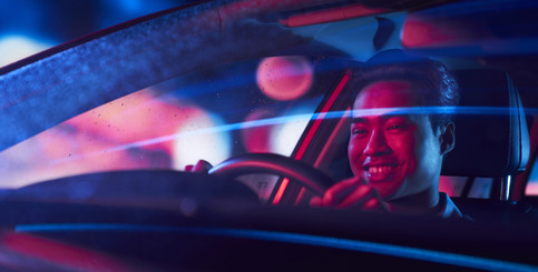 A smiling young man driving an electric car at night