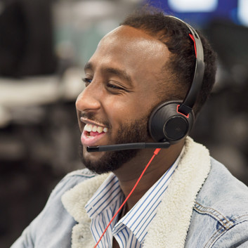 A man laughing while he talks on a headset, in an office