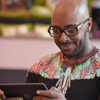 A man with glasses smiling while reading an iPad